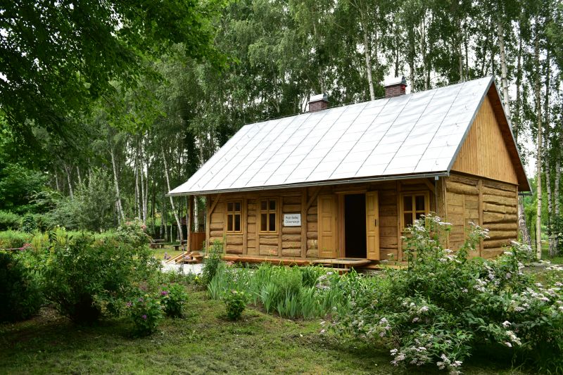 widok na drewniany dom podcieniowy przeniesiony z Kalwarii Pacławskiej na tle zasianego ogródka warzywnego