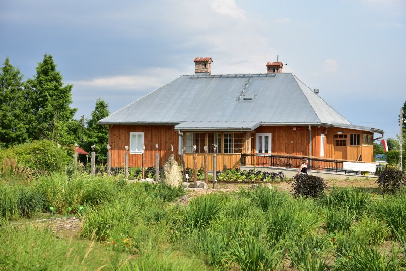 budynek zabytkowej drewnianej Plebanii z Jodłówki nakryty dachem czterospadowym z trzema werandamina tle roślinności