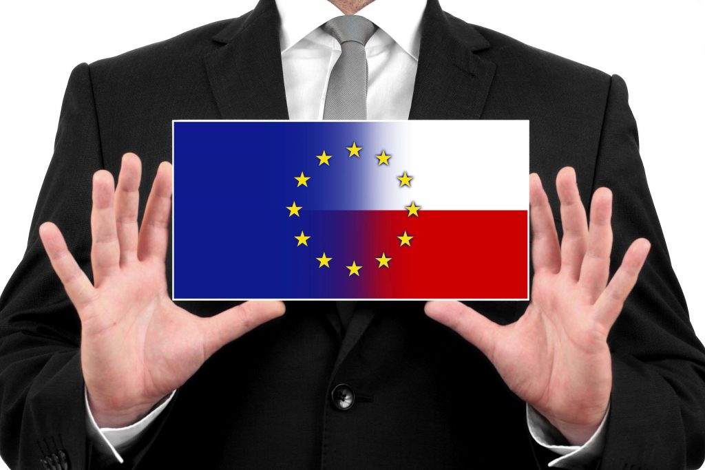 mężczyzna w garniturze trzyma w rękach obrazek, na których w połpowie jest flaga unijna i flaga Polski
