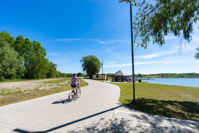 rowerzystka na drodze rowerowej nad Jeziorem Tarnobrzeskim, w tle altanka