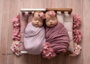dwa niemowlaki owiniete w różowe beciki ułożone na maych łóżeczkach