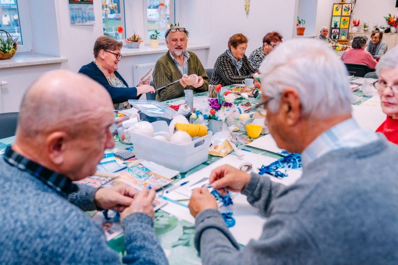 grupa starszych osób wykonuje prace ręczne przy współnym stole