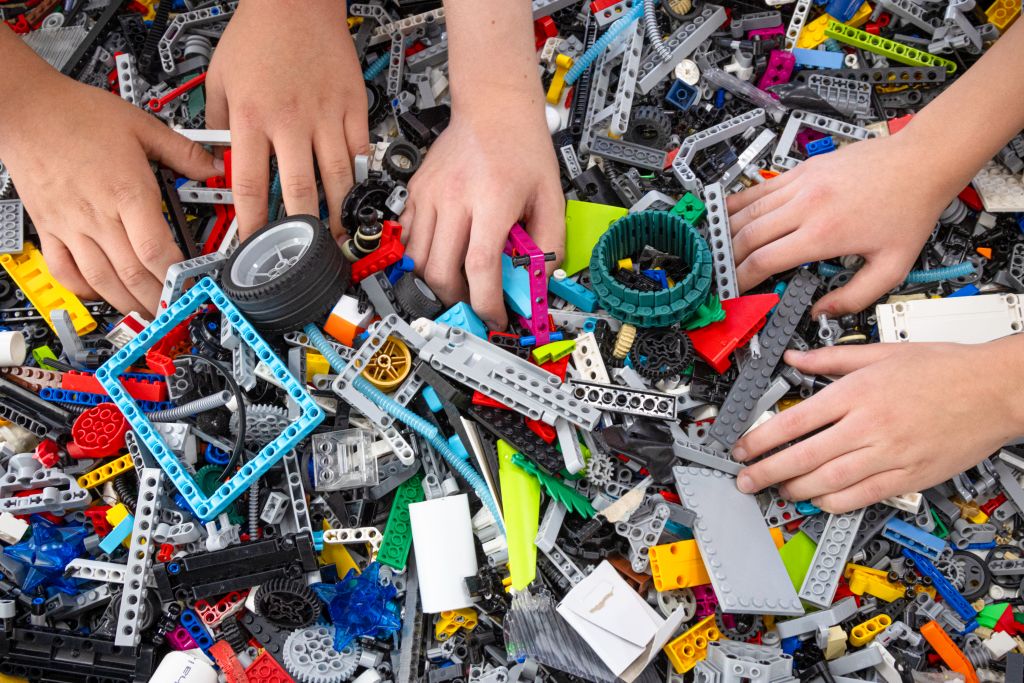 Dziecięce ręce zabierają i sortują kolorowe klocki LEGO z dużego stosu. Klocki są różnego kształtu, rozmiaru i koloru.