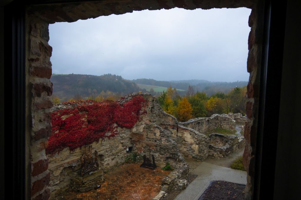 Widok z okna na jesienny krajobraz i fragmenty murów.